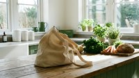 Eco-friendly reusable shopping bag with fresh organic vegetables on wooden kitchen counter promoting sustainable zero waste lifestyle.