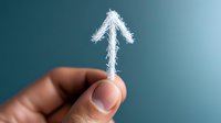 Upward pointing arrow made of white frost crystals held between fingers against blue background, symbolizing growth, progress and winter business concept.