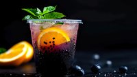 Refreshing dark purple cocktail with orange slice, mint leaves and ice cubes on black background. Carbonated beverage with bubbles and garnish for bar menu.