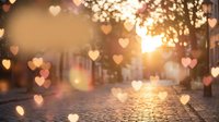 Romantic cobblestone street at sunset with floating heart-shaped bokeh lights creating dreamy atmosphere for Valentine's Day and love concepts.