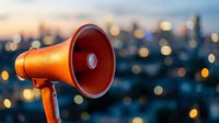 Orange megaphone against blurred city lights at dusk for communication, announcement, marketing campaigns, public speaking, and business promotion.