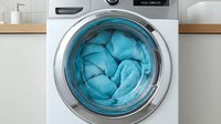 Modern washing machine drum filled with blue laundry items in contemporary white kitchen interior for household appliance and cleaning concepts.