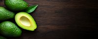 Fresh ripe avocados with green leaves on dark wooden background, half cut showing creamy flesh. Copy space for menu or recipe design.