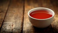 Red tomato soup in white ceramic bowl on rustic wooden table background with dramatic lighting and copy space for menu design.