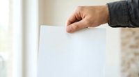 Man in dark jacket holding blank white paper sheet, voting ballot, or document for election, survey, or business presentation purposes.