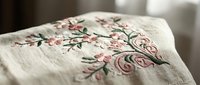 Delicate pink floral embroidery on natural linen fabric with intricate rose and branch patterns for crafting and textile design projects.