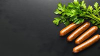 Grilled sausages with fresh parsley leaves on dark black background with copy space. Food photography for menu, restaurant promotion and cooking.