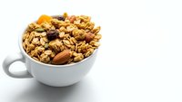 Healthy breakfast granola with nuts, dried fruits and oats in white ceramic cup on clean background for morning meal and nutrition concepts.