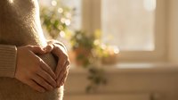 Woman in cozy beige sweater holding warm mug by sunny window with soft bokeh lights creating peaceful morning atmosphere for relaxation and comfort.