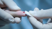 Medical professional in white gloves performing blood glucose test with lancet device on patient finger showing red blood drop for diabetes monitoring.
