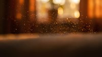 Golden dust particles floating in warm ambient light with blurred background bokeh creating magical atmospheric effect for luxury product displays.