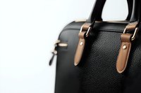 Luxury black leather handbag with brown leather straps and metal buckles shown in close-up detail against white background, highlighting quality materials and craftsmanship.