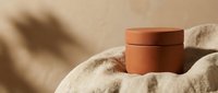 Terracotta cosmetic jar on soft beige fabric with palm shadow, minimalist beauty product mockup for skincare branding and natural cosmetics packaging design.