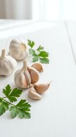 Fresh garlic bulbs and cloves with green parsley leaves arranged on white wooden surface for culinary cooking and healthy food preparation.