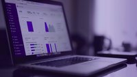 Modern laptop displaying analytics dashboard with purple graphs and charts on screen, workspace setting with blurred background in cool tones.