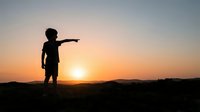 Young child silhouette pointing toward sunset sky during golden hour. Outdoor adventure and exploration concept for children's education and inspirational content.