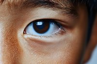 Close-up macro shot of Asian male brown eye with detailed view of iris, pupil and eyelashes against smooth skin texture. Natural lighting highlights eye detail.