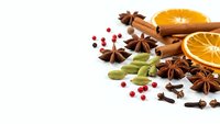 Aromatic winter spices with orange slices, cinnamon sticks, star anise, cardamom pods and pink peppercorns on white background for holiday cooking.