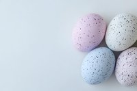 Pastel speckled Easter eggs in pink, blue and white arranged on light background, minimal holiday composition with copy space for seasonal designs.