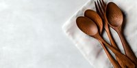 Wooden spoons and forks on white linen napkin against light marble background, minimalist eco-friendly kitchen utensils for sustainable dining and food styling.
