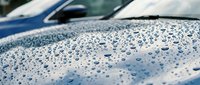 Water droplets on car hood surface after rain with blurred vehicle background showing automotive detailing and weather protection concepts.