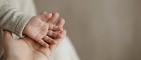 Tiny newborn hand resting on adult palm, soft neutral background with copy space, symbolizing care, love, and new life.