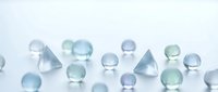 Collection of translucent glass spheres and geometric shapes in soft blue and green tones scattered on white surface for modern design projects.