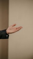 Open palm of a Caucasian male professional wearing a dark suit and silver bracelet, gesturing in offering or presentation pose against neutral beige background.