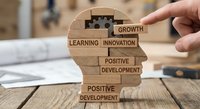 Hand placing wooden puzzle piece labeled growth into human head silhouette with business development concepts on office desk for corporate training materials.