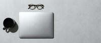 Minimalist workspace flat lay with laptop, coffee mug, and glasses on gray concrete desk, copy space for business or creative use.