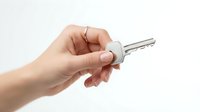 Hand holding silver house key on white background isolated for real estate and property concepts.
