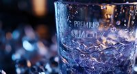 Frosted glass with premium quality text engraved, surrounded by ice cubes and water droplets in blue tones with bokeh background lighting effects.