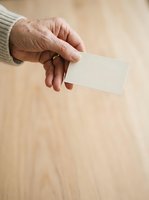 Senior male hand holding blank white business card against wooden surface for corporate branding and marketing mockup presentations.