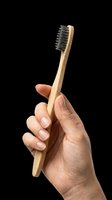 Female hand holding an eco-friendly bamboo toothbrush with charcoal bristles, isolated on transparent background. For stickers, print on demand, and T-shirt design.