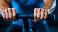 Close-up of hands gripping black handlebar of exercise equipment against blue background, showing determination and focus during fitness workout.