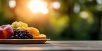 Fresh seasonal fruits on wooden table at sunset with natural bokeh background, including red apple, grapes, oranges and bananas, creating healthy food composition.