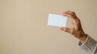 Male hand holding blank white business card against neutral beige background, suitable for branding, corporate identity, and marketing mockup designs.