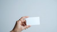 Hand holding blank white business card mockup against gray background for branding and corporate identity design projects.