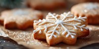 Star-shaped gingerbread cookies with white icing snowflake patterns dusted with powdered sugar on parchment paper for holiday baking and festive celebrations.