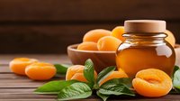 Fresh apricots with green leaves and glass jar of honey on rustic wooden background, natural organic ingredients for healthy eating and wellness.