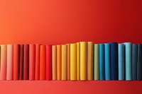 Colorful row of books arranged in rainbow spectrum from pink to blue against vibrant red background, creating visual gradient for education or library concepts.