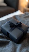 Elegant black gift box with satin ribbon bow on dark textile background, soft ambient lighting creates luxurious mood for special occasions and celebrations.