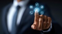 Professional in dark suit touching virtual interface with glowing icons representing banking, communication and business services on black background.