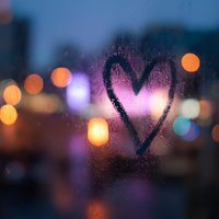 Heart shape drawn on foggy window glass with colorful bokeh city lights in background creating romantic atmosphere for love concepts.