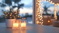 Glowing candles in glass holders and potted plant on table with blurred festive lights and winter window view creating cozy evening atmosphere.