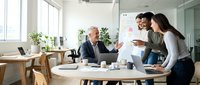 Diverse business team collaborating at whiteboard in modern office space, discussing strategy and ideas during creative brainstorming session.
