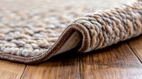 Close up view of rolled carpet edge showing texture and layers of beige wool rug on wooden floor, demonstrating quality flooring materials and home interior details.