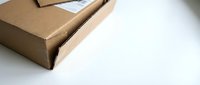 Brown cardboard shipping box with white label on clean white surface for e-commerce delivery and packaging concepts.