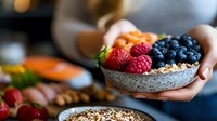 Fresh berries and granola in stone bowl held by hands against dark background, healthy breakfast with raspberries, blueberries and strawberries.