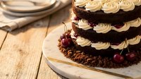 Decadent chocolate layer cake with cream frosting and cherry garnish on rustic wooden table, perfect for celebrations and dessert photography.